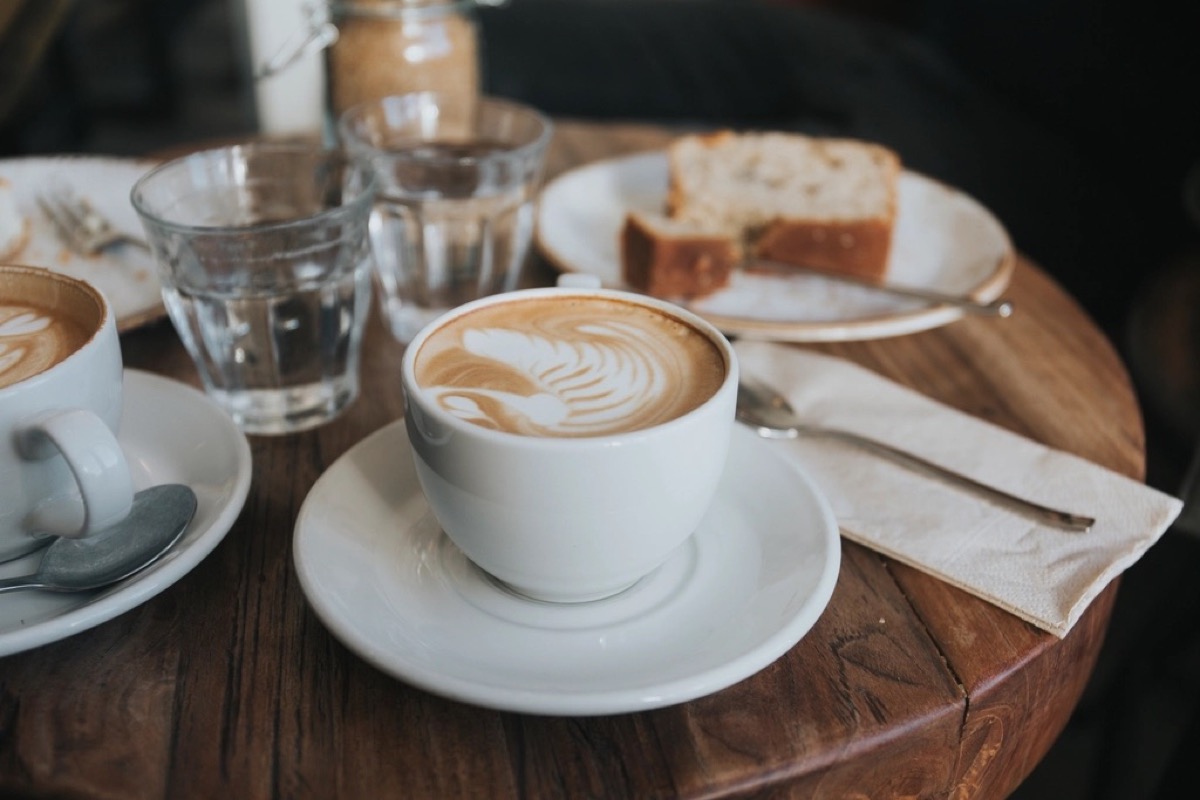Een kop cappuccino met een schaaltje cake op een houten tafel