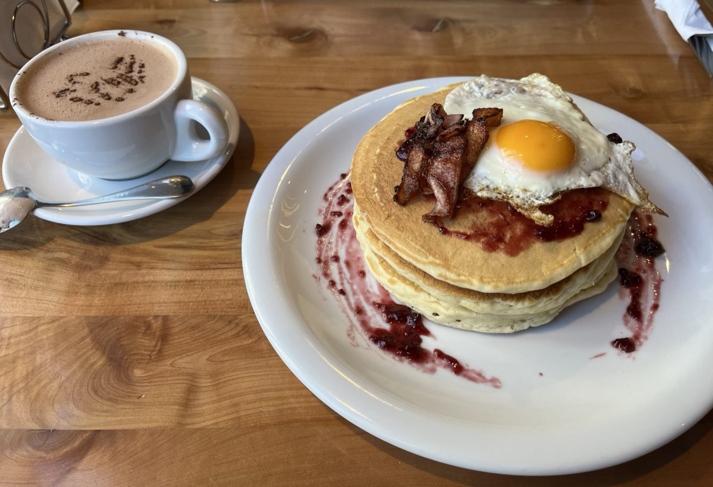 Een stapel pannenkoeken op een bord naast een kop koffie op een houten tafel